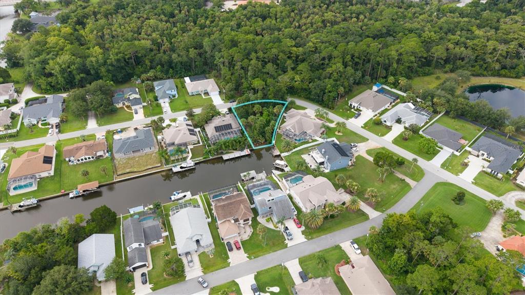 An aerial view shows a residential neighborhood with houses bordering a canal and a wooded area — 27 COLECHESTER LANE, PALM COAST, FL