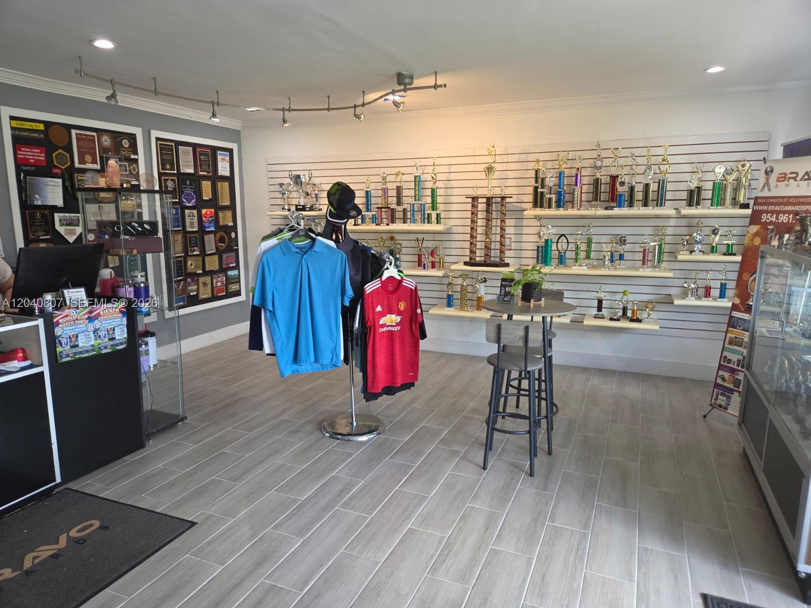 A retail shop displays numerous trophies on wall shelves alongside clothing racks and a table — 5824 Johnson St, Hollywood FL 33021, HOLLYWOOD, FL