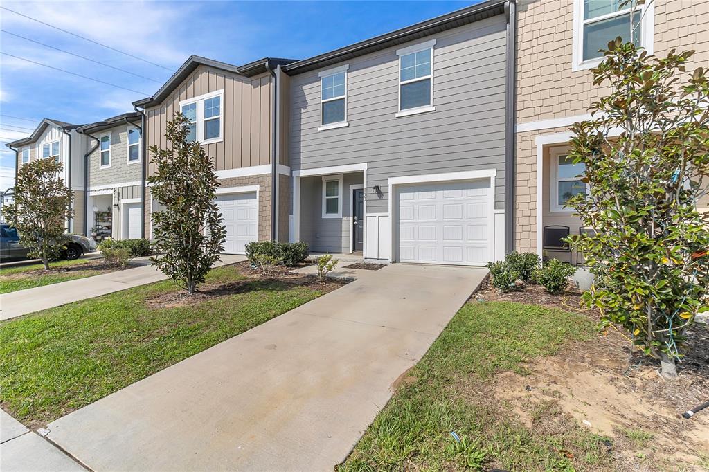A row of two-story townhomes with gray siding, attached garages, and concrete driveways — 153 MANDOVI STREET, DAVENPORT, FL