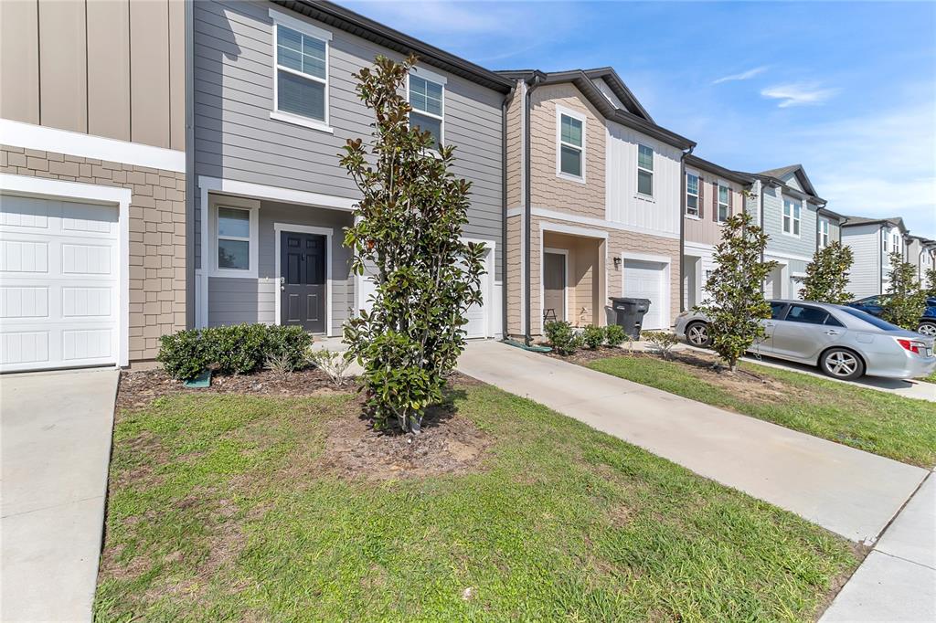 A row of two-story townhouses with gray and tan siding, concrete driveways, and small front lawns — 153 MANDOVI STREET, DAVENPORT, FL