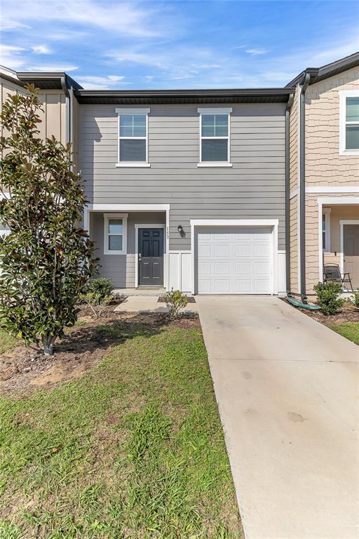 A two-story townhouse features gray horizontal siding, a single-car garage, and a concrete driveway — 153 MANDOVI STREET, DAVENPORT, FL