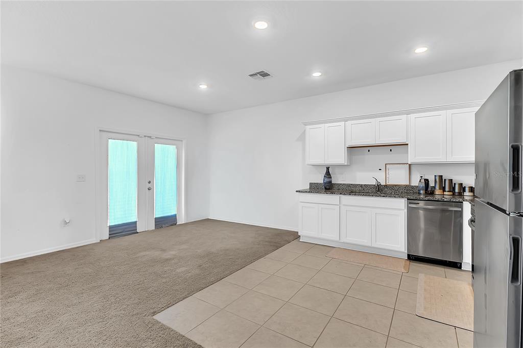 A kitchen with white cabinets and tile flooring adjacent to a carpeted living area — 153 MANDOVI STREET, DAVENPORT, FL