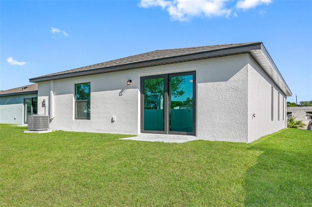 The exterior of a white stucco house features a sliding glass door and a lawn — 543 BLACKTHORN DRIVE, LAKELAND, FL