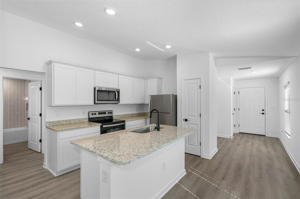 A kitchen with white cabinets, granite countertops, a center island, and light wood-look flooring — 543 BLACKTHORN DRIVE, LAKELAND, FL