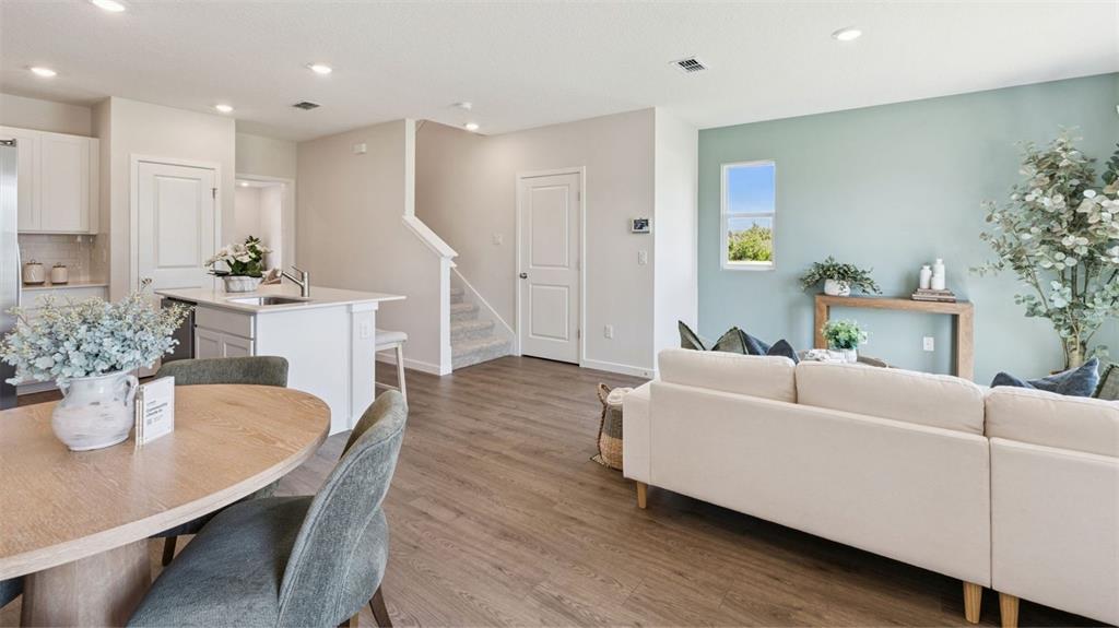 An open-concept living and dining area features wood-look flooring, a kitchen island, and stairs — 2247 RITA LANE, KISSIMMEE, FL