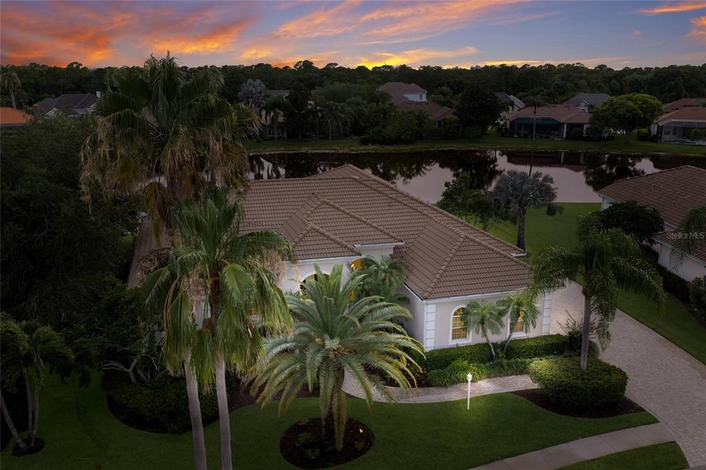 An aerial view shows a single-story house with a tiled roof, palm trees, and lake — 7920 ROYAL QUEENSLAND WAY, LAKEWOOD RANCH, FL