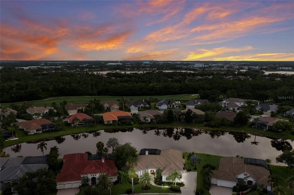 An aerial view shows a suburban neighborhood with houses surrounding a lake at sunset — 7920 ROYAL QUEENSLAND WAY, LAKEWOOD RANCH, FL