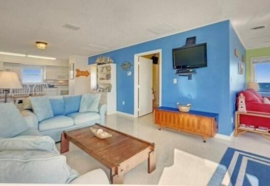A living room features blue walls, a light blue sofa, a wooden coffee table, and television — 1501 NE Ocean Boulevard # 2, Stuart FL 34996, STUART, FL