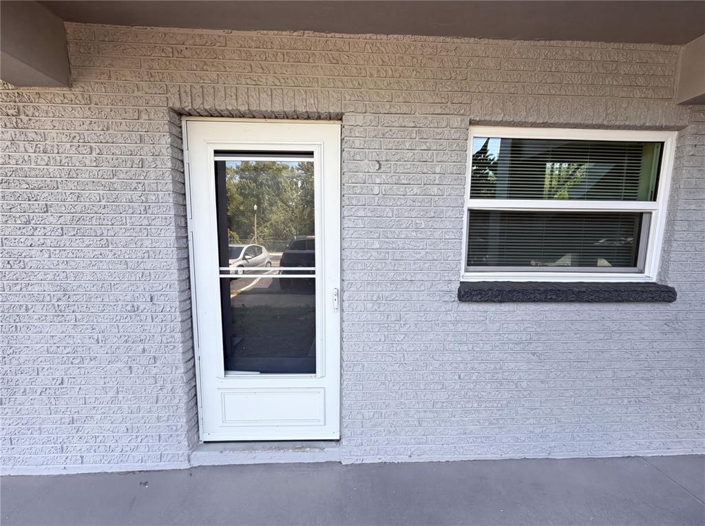 A white storm door and a window are set into a gray painted brick wall — 1303 S HERCULES AVENUE UNIT 6, CLEARWATER, FL