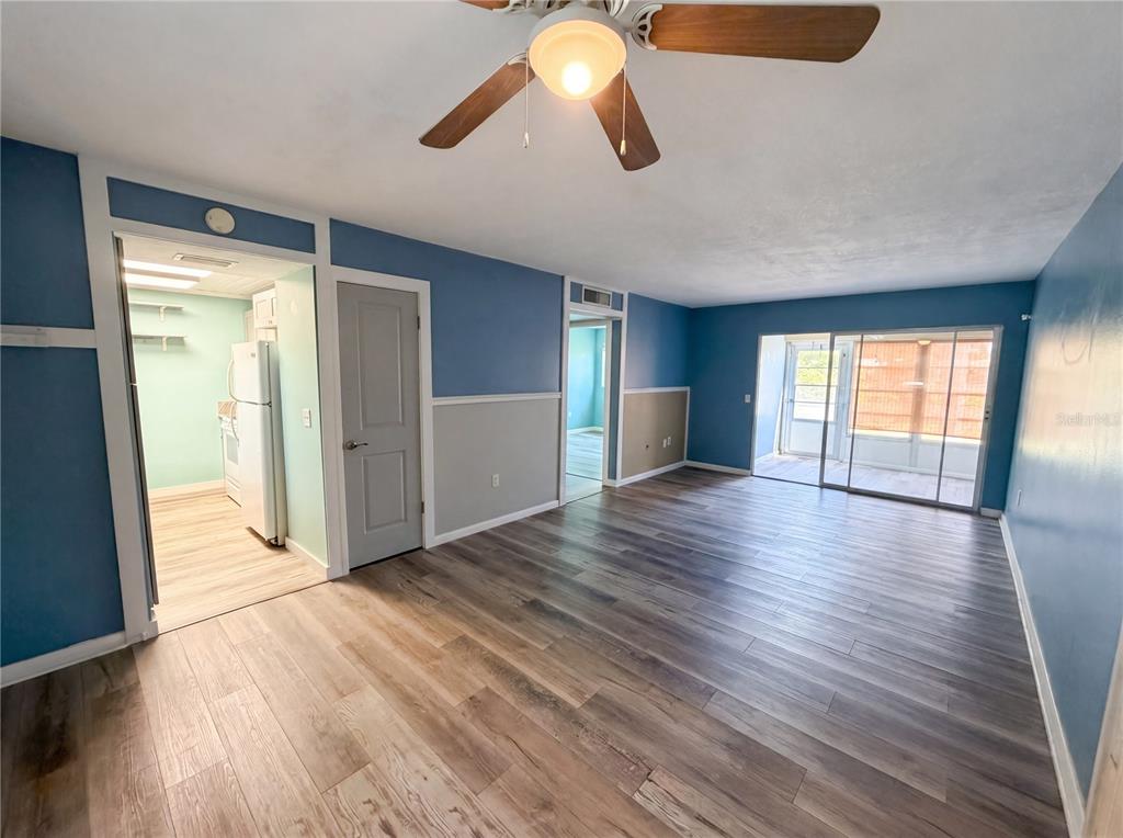 A living room with blue walls, wood-look flooring, a ceiling fan, and a sliding glass door — 1303 S HERCULES AVENUE UNIT 6, CLEARWATER, FL