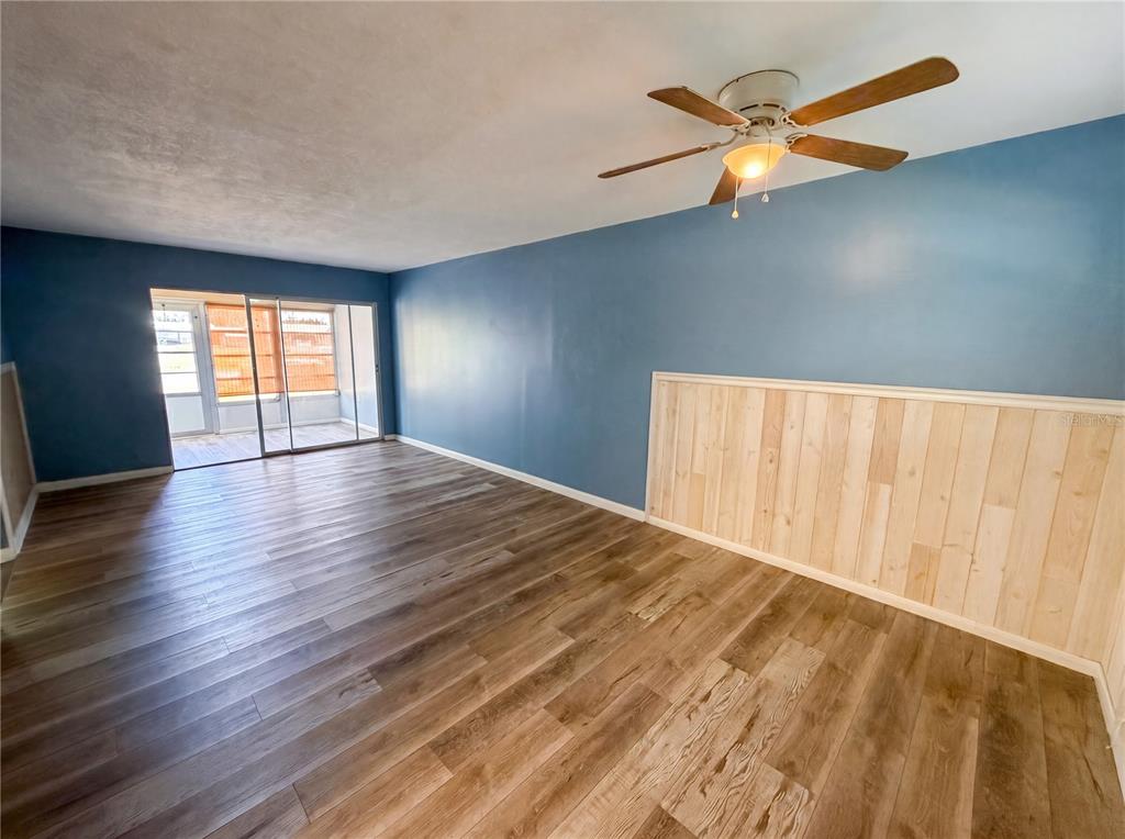 A living room with blue walls, wood-look flooring, a ceiling fan, and wood wainscoting — 1303 S HERCULES AVENUE UNIT 6, CLEARWATER, FL
