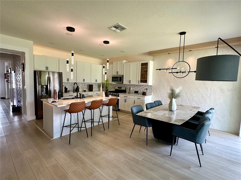 A modern kitchen and dining area with white cabinetry, a marble island, and pendant lighting — 13518 PARKFIELD WAY, WINTER GARDEN, FL