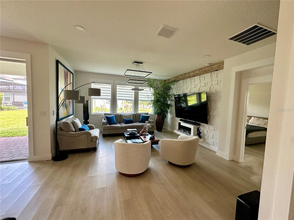 A living room features light wood floors, a textured white accent wall, and a large television — 13518 PARKFIELD WAY, WINTER GARDEN, FL
