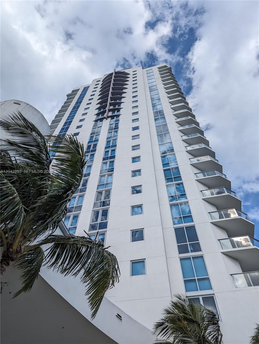 A low-angle view of a tall white residential building with balconies and palm trees — 17111 E Biscayne Blvd # 1011, North Miami Beach FL 33160, NORTH MIAMI BEACH, FL