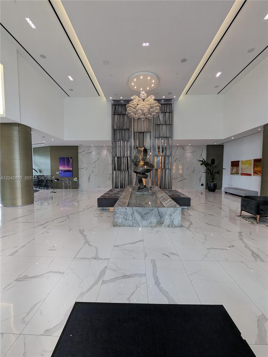 A modern lobby features white marble floors, a central water feature, and a sculptural chandelier — 17111 E Biscayne Blvd # 1011, North Miami Beach FL 33160, NORTH MIAMI BEACH, FL