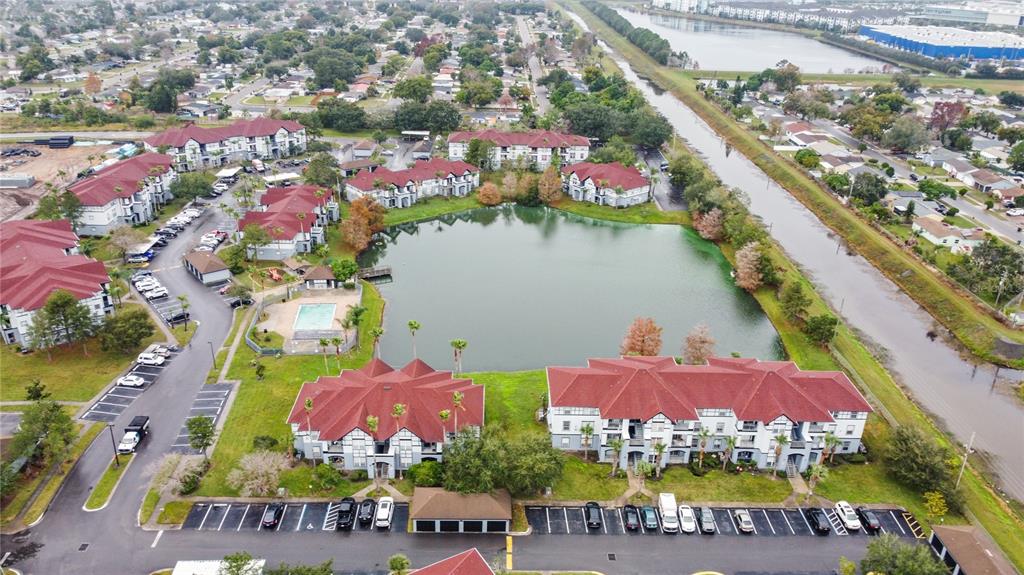 An aerial view shows apartment buildings with red roofs surrounding a central pond and pool — 3725 CASTLE PINES LANE UNIT 4322, ORLANDO, FL