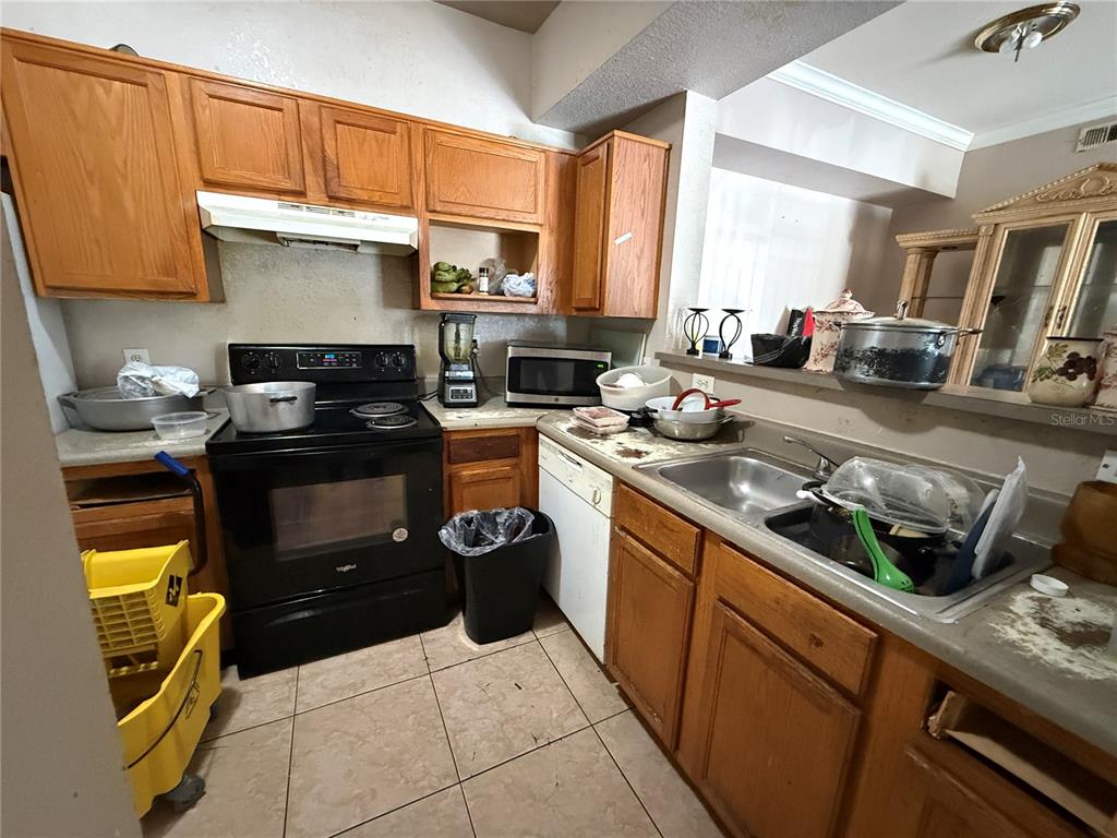 A kitchen features wood cabinets, a black stove, a stainless steel sink, and tile flooring — 3725 CASTLE PINES LANE UNIT 4322, ORLANDO, FL