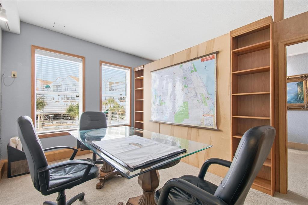 A home office features a glass-topped desk, black chairs, built-in wooden shelving, and a wall map — 101 PALM HARBOR PARKWAY UNIT OB2, PALM COAST, FL