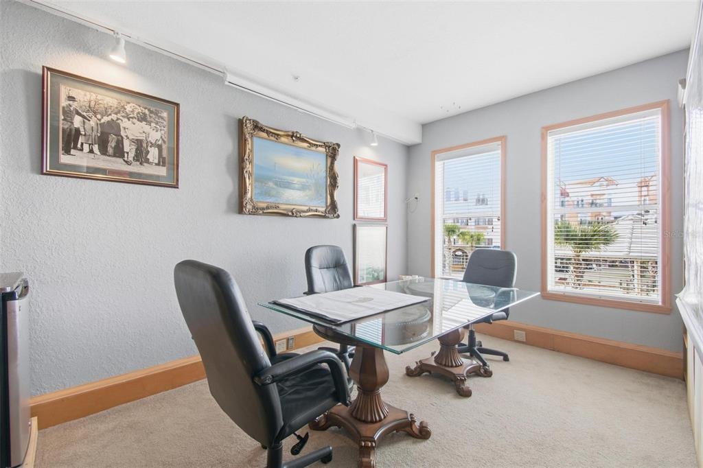 A home office features a glass-topped table, three black chairs, and framed wall art — 101 PALM HARBOR PARKWAY UNIT OB2, PALM COAST, FL