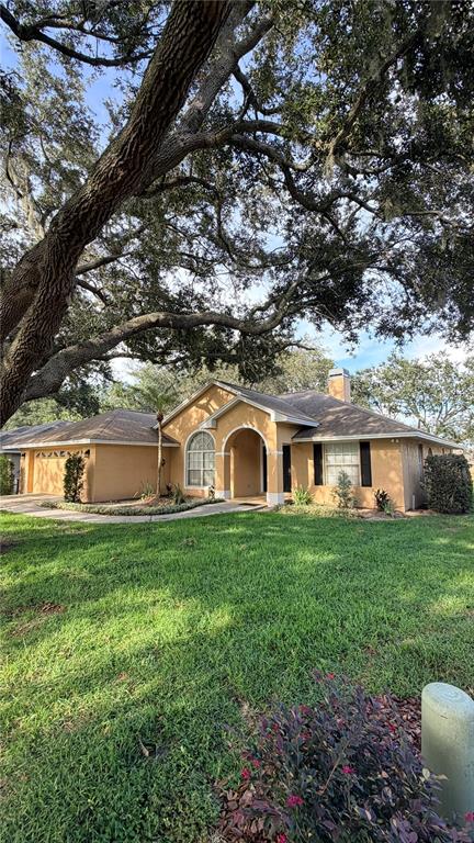 A single-story tan house with a shingled roof sits under a large oak tree — 2782 HIGH RIDGE DRIVE, LAKELAND, FL