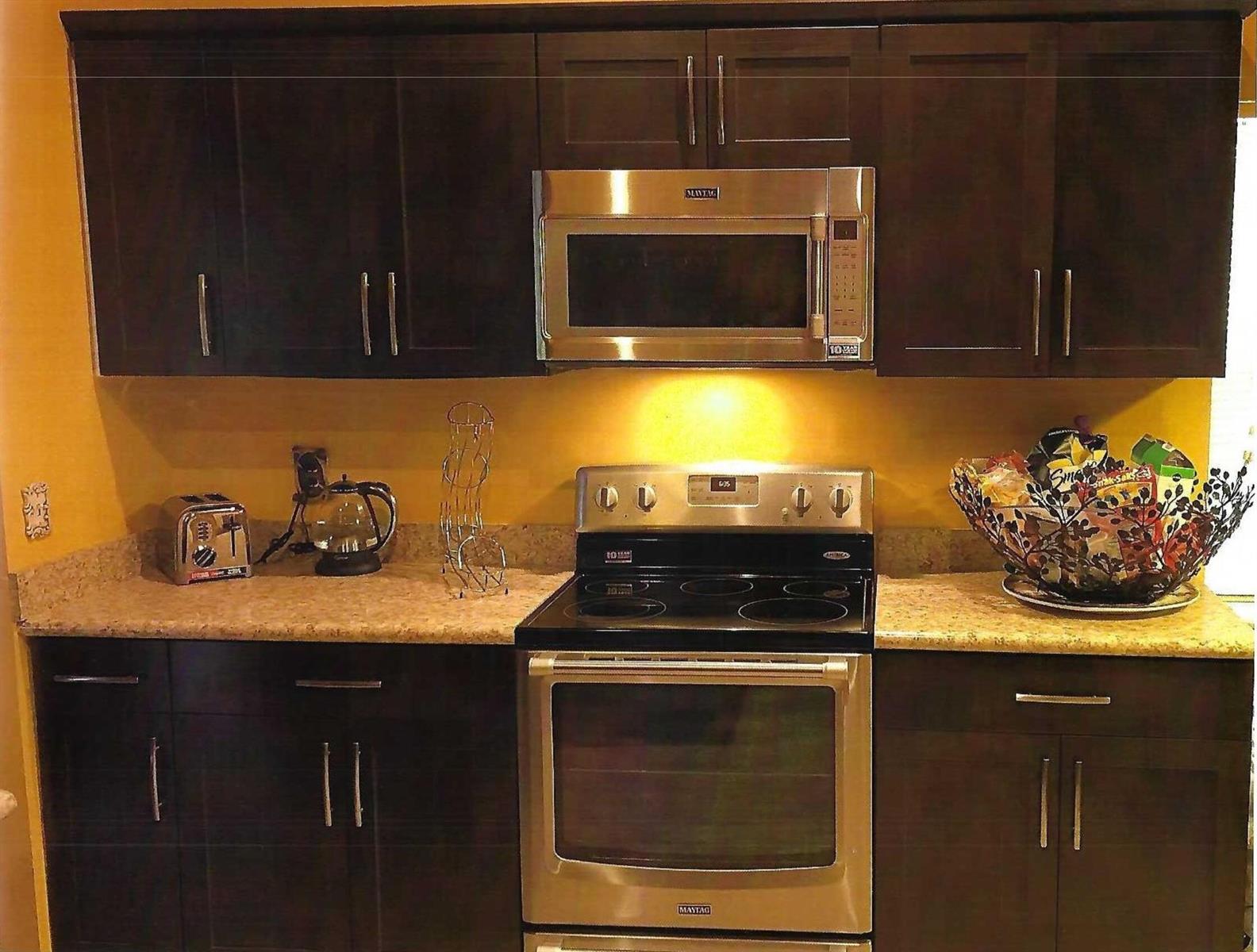 A kitchen features dark wood cabinets, stainless steel appliances, and a tan speckled countertop — 8862 Jaspers Drive, Boynton Beach FL 33472, BOYNTON BEACH, FL