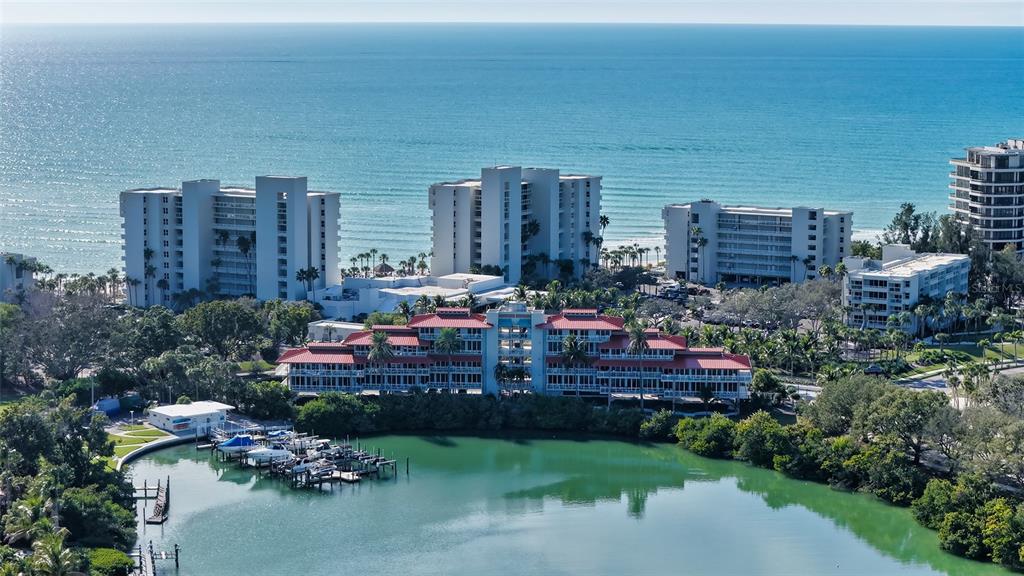 An aerial view shows a multi-story building with a red roof beside a boat marina — 225 SANDS POINT ROAD UNIT 6201, LONGBOAT KEY, FL