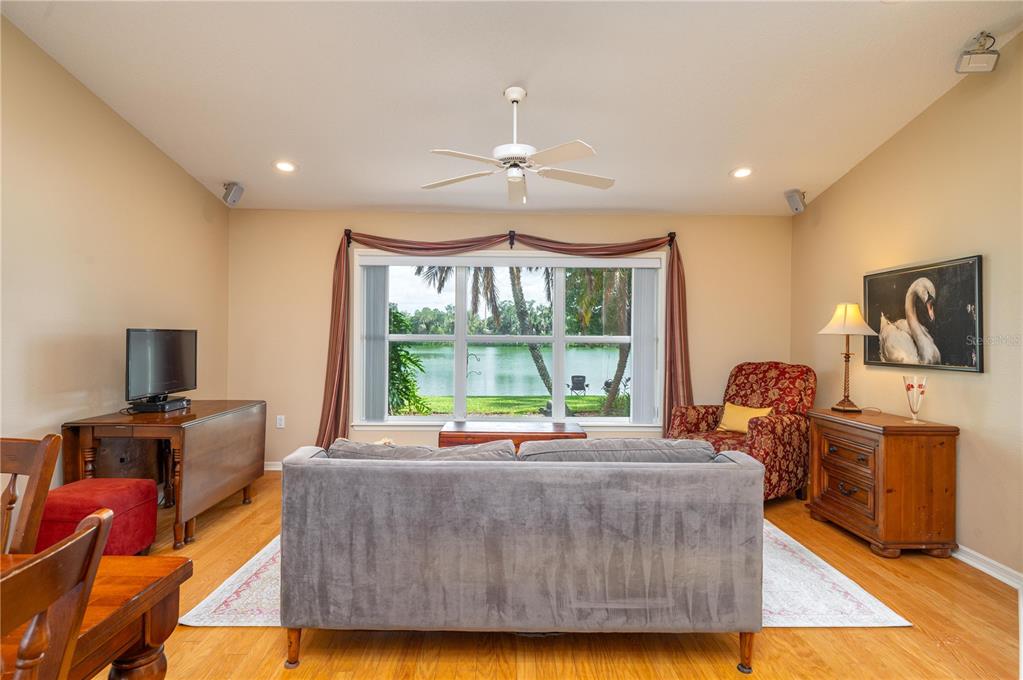 A living room with a gray sofa, patterned armchair, ceiling fan, and a view of water — 5667 WATER OAK LANE, MULBERRY, FL