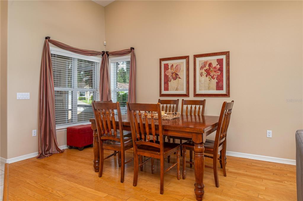 A dining room with a wooden table, four chairs, hardwood floors, and two framed floral prints — 5667 WATER OAK LANE, MULBERRY, FL