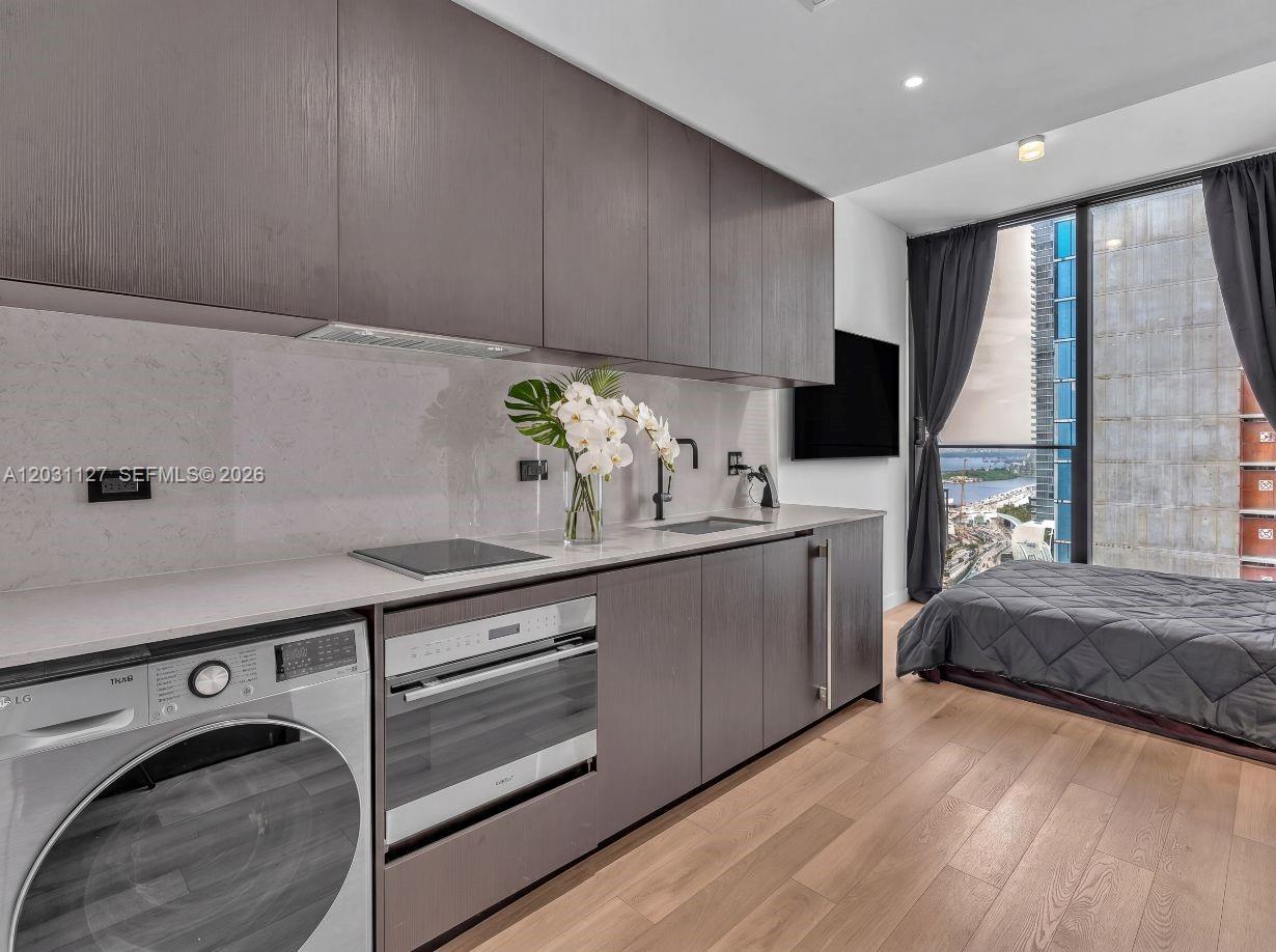 A studio apartment features a kitchenette with dark cabinetry, integrated appliances, and a bed nearby — 20 NE 11th St # 3106B, Miami FL 33132, MIAMI, FL