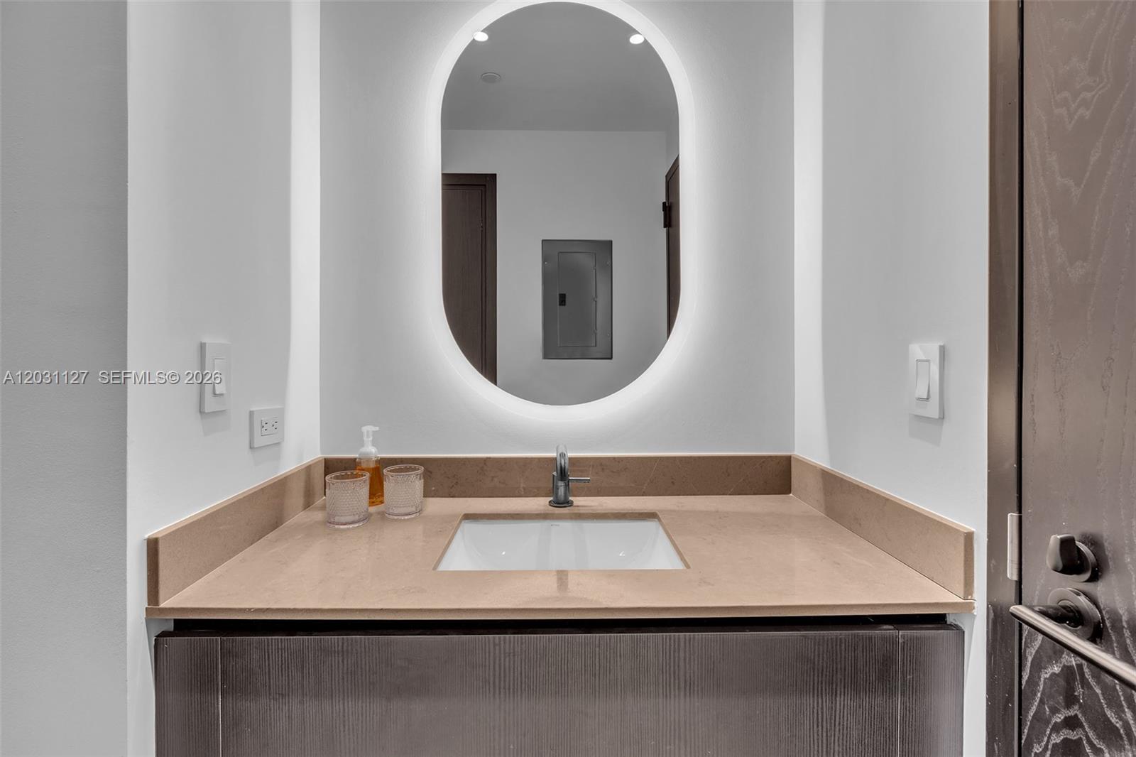 A modern bathroom features a dark vanity, a tan countertop, and an oval backlit mirror — 20 NE 11th St # 3106B, Miami FL 33132, MIAMI, FL