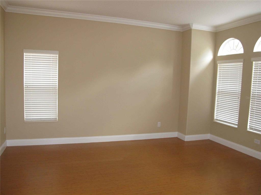 An empty room with light-colored walls, wood-look flooring, and several windows with white blinds — 6828 LUCCA STREET, ORLANDO, FL
