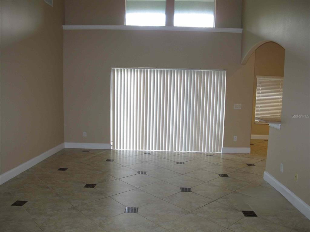 An empty room features beige tile flooring, high ceilings, and large sliding glass doors — 6828 LUCCA STREET, ORLANDO, FL