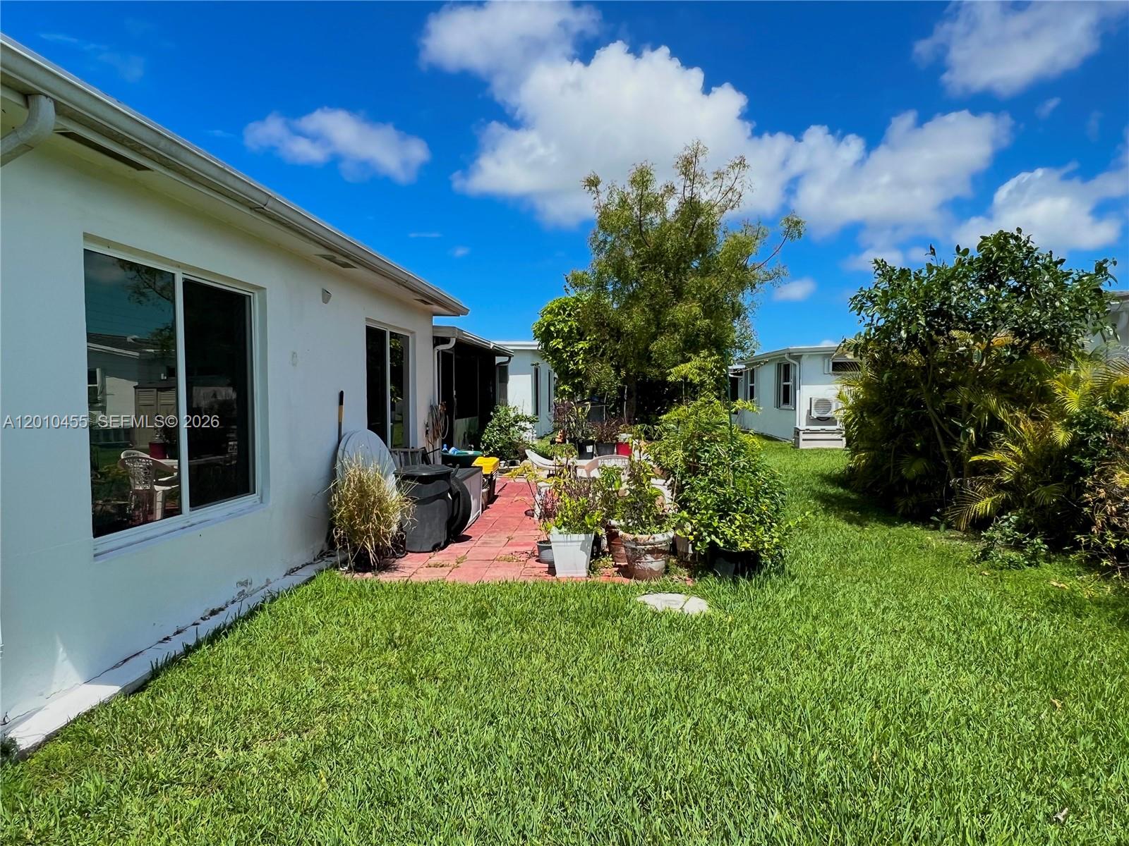 A white house exterior features a patio area with potted plants and a grassy yard — 6800 NW 15th St, Margate FL 33063, MARGATE, FL