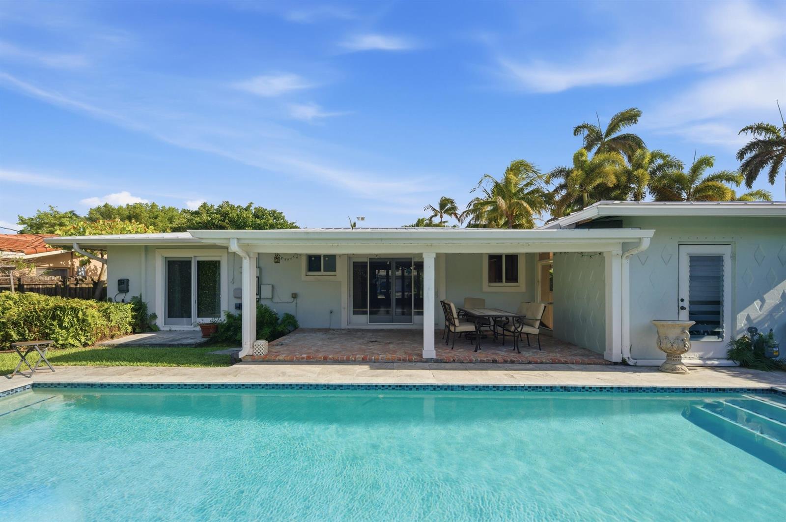 A backyard swimming pool sits in front of a house with a covered patio area — 2685 SE 6th Street, Pompano Beach FL 33062, POMPANO BEACH, FL