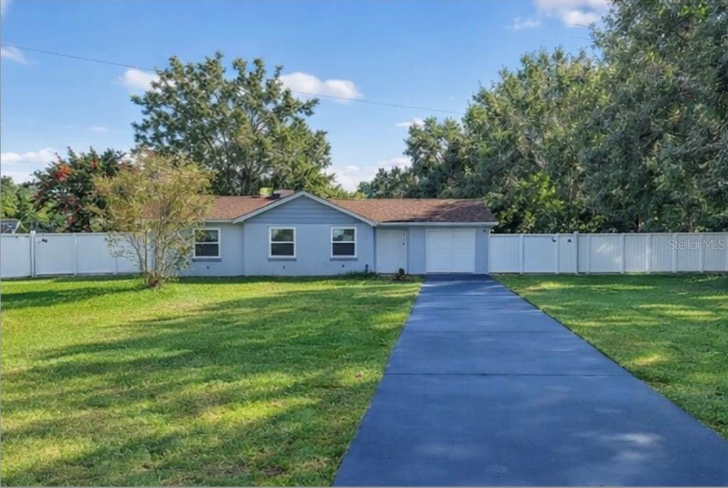 A single-story light blue house with a white garage door and a long paved driveway — 3536 EAGLES NEST ROAD, FRUITLAND PARK, FL