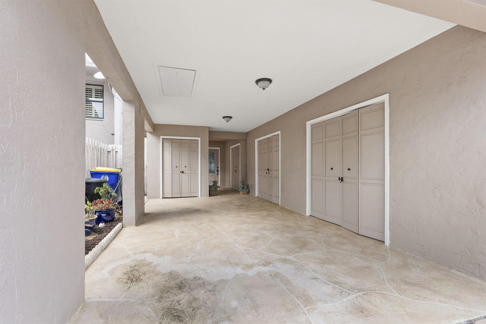 A covered patio area features light-colored stone flooring, beige walls, and several sets of storage doors — 4189 SE Saint Lucie Boulevard, Stuart FL 34997, STUART, FL
