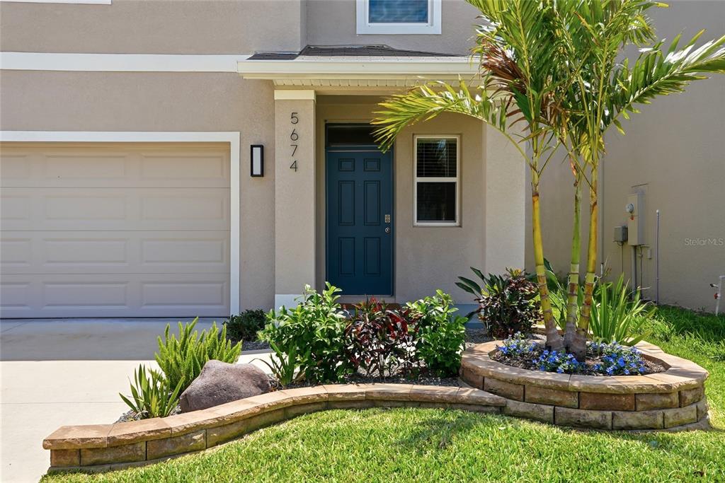 The exterior of a two-story home features a blue front door and a stone planter — 5674 CHORLEYWOOD LANE, WESLEY CHAPEL, FL