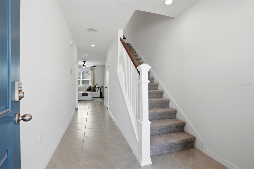 A tiled entryway features a carpeted staircase with a white railing and a hallway leading forward — 5674 CHORLEYWOOD LANE, WESLEY CHAPEL, FL