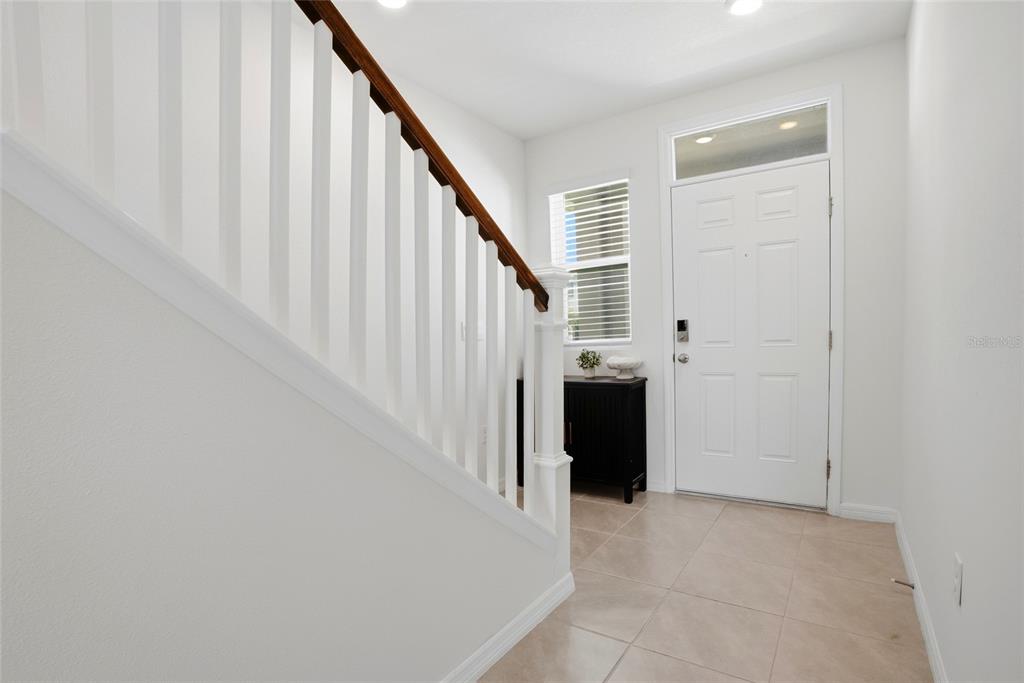 An entryway features a staircase with a wooden handrail, tile flooring, and a white door — 5674 CHORLEYWOOD LANE, WESLEY CHAPEL, FL