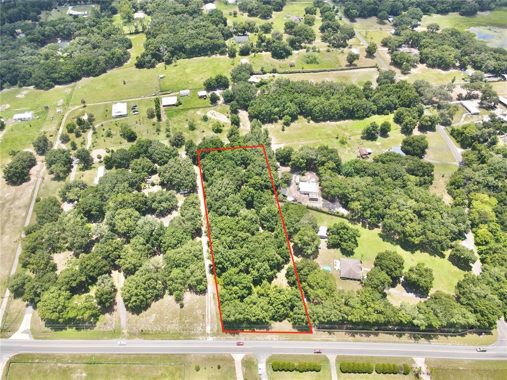 An aerial view shows a rectangular, tree-covered vacant lot outlined in red along a road — SE HWY 42, WEIRSDALE, FL