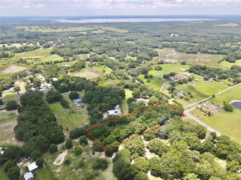 An aerial view shows a rectangular, tree-covered lot outlined in red next to a road — SE HWY 42, WEIRSDALE, FL