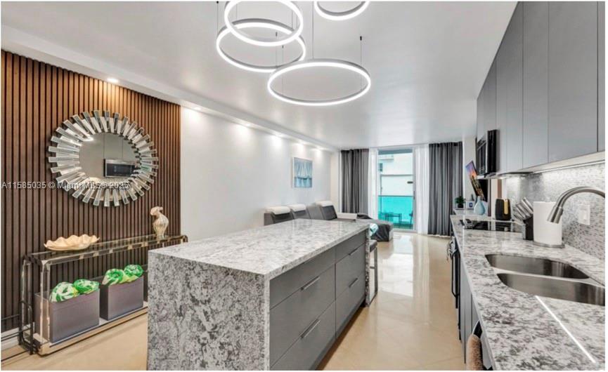 A modern kitchen features a granite island, gray cabinetry, and a sunburst mirror on wood-slatted walls — 4001 S Ocean Dr # 3L, Hollywood FL 33019, HOLLYWOOD, FL