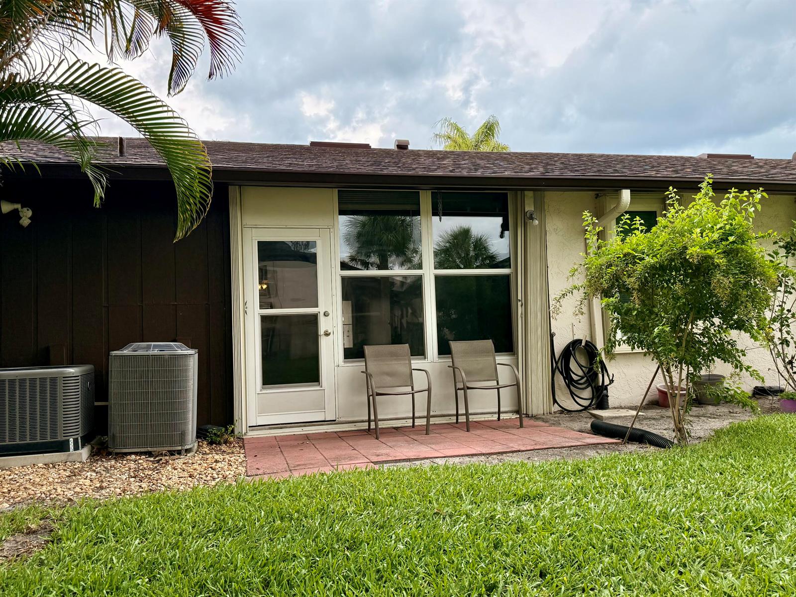 A patio with two chairs sits outside a glass door and windows of a house — 6531 SE Federal Hwy # 107, Stuart FL 34997, STUART, FL