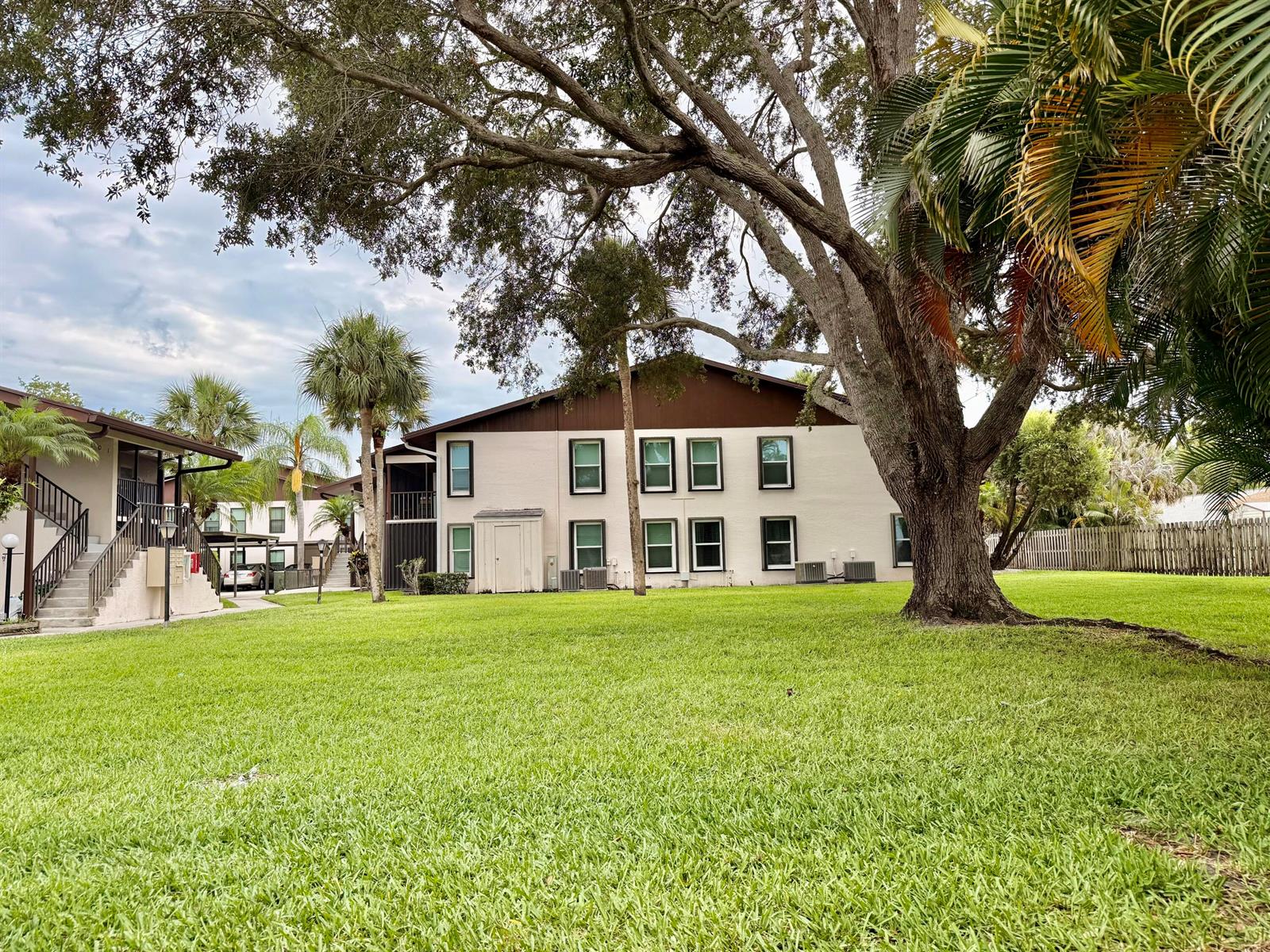 A two-story apartment building with a large lawn and mature trees in the foreground — 6531 SE Federal Hwy # 107, Stuart FL 34997, STUART, FL