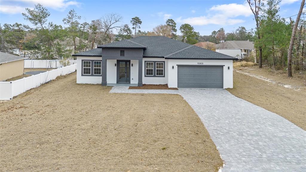 A single-story house with a white exterior, dark gray roof, and a paved driveway — 15303 SW 48TH AVENUE, OCALA, FL