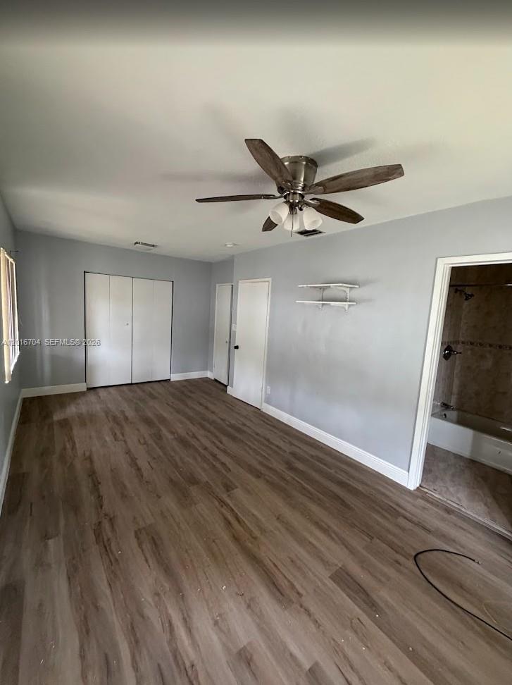 A bedroom with light gray walls, wood-look flooring, a ceiling fan, and an attached bathroom — MIAMI, FL