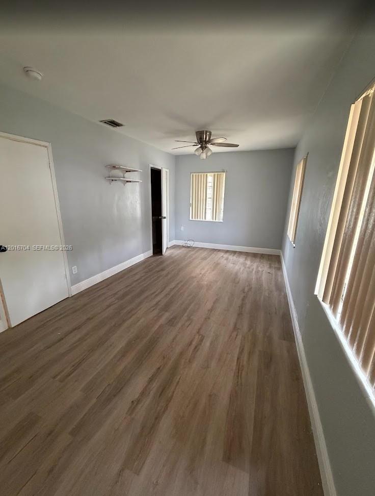 An empty room features light gray walls, wood-look flooring, a ceiling fan, and vertical blinds — MIAMI, FL