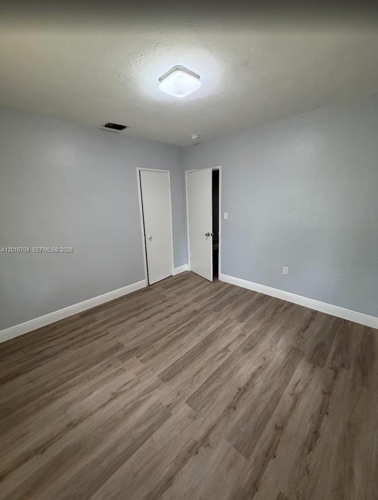 An empty bedroom features light gray walls, wood-look flooring, and two white doors — MIAMI, FL