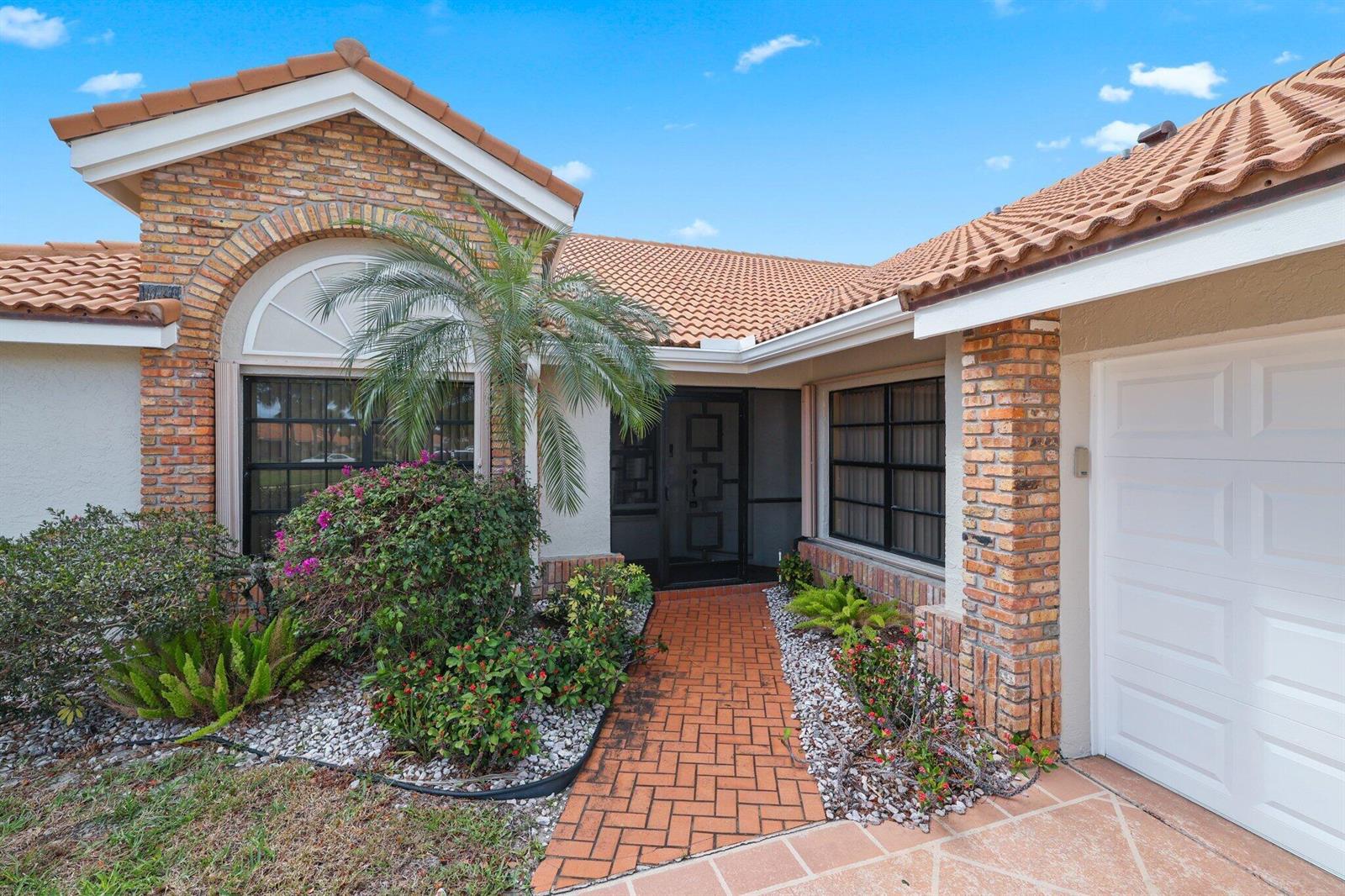 The exterior of a single-story house features a brick facade, tile roof, and brick walkway — 8423 Juddith Avenue, Boynton Beach FL 33472, BOYNTON BEACH, FL