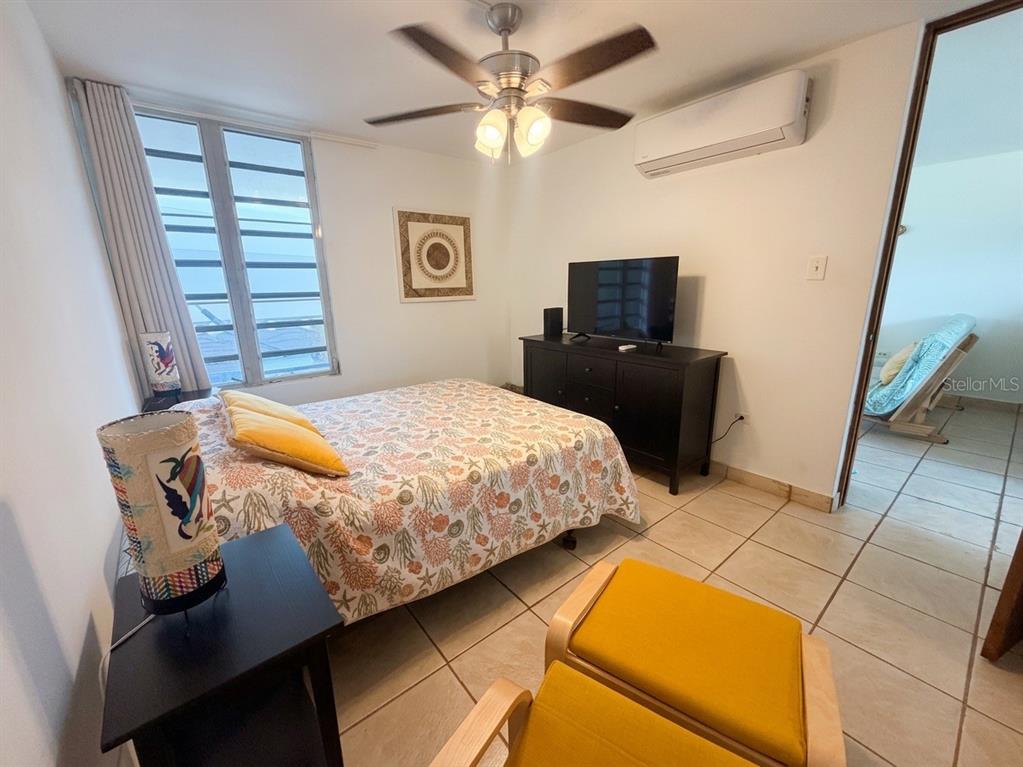 A bedroom features a bed with a coral-patterned quilt, a television, and tile flooring — #16 COND. PARGUERA SUITES, LAJAS, PR